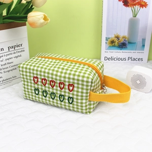 Detail of green checkered makeup bag with red heart embroidery and yellow zipper handle