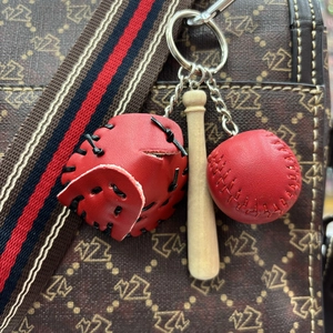 Close-up of mini red leather baseball glove, wooden bat and ball keychain charm on bag
