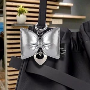 Silver puffy bow and heart pendant bag charm hanging on a black handbag with spring clasp