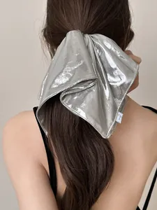 Silver metallic oversized bow hair scrunchie shown on a ponytail with a white brand label
