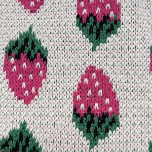 Macro shot of knitted strawberry pattern on white fabric showing detailed texture