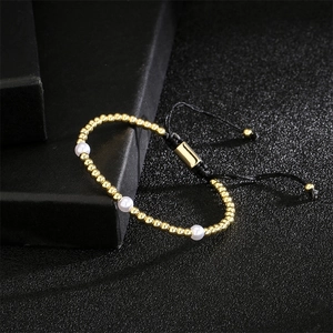 Détail du bracelet perlé doré avec perles et cordon noir réglable sur un coffret noir