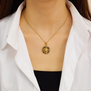 Detalle de un collar de acero de titanio dorado con colgante de brújula negra en una modelo