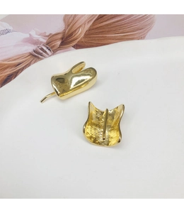 Close-up of polished gold alloy stud earrings on a white ceramic tray with metal texture