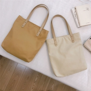 Flat lay detail of mustard and cream minimalist tote bags with golden rivets on white bedding