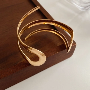 Dettaglio macro del bracciale aperto dorato lucido su un supporto in legno minimalista