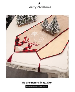 Close-up of burlap Christmas table runner with embroidered elk, snowflakes, and red tassels