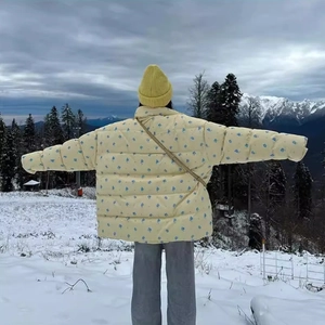 Women's light yellow hooded puffer jacket with blue floral print in a snowy landscape