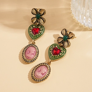 Close-up of vintage earrings with green enamel and pink relief portrait on beige surface