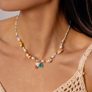 Detail of bohemian shell and pearl beaded necklace with gold heart and blue tassel