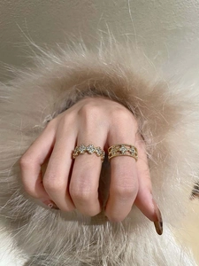 Detail of gold clover rings with zircon inlay worn on hand over beige fur cuff