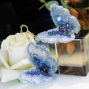 Sparkling butterfly earrings with light blue crystals and gold hooks on white roses