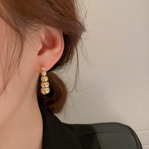 Detail of elegant gold bead earrings showing metallic luster on model ear