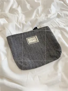 Close-up of checkered fabric makeup bag with Pleasant Time logo on white bedding
