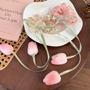 Pink and beige tulip flower hair scrunchies with green ribbons on a wooden background