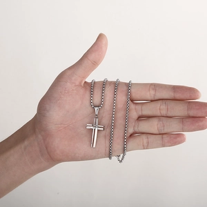 Close-up of a silver hollow 3D cross pendant on a box chain held in hand