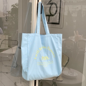 Detail of light blue canvas tote bag with yellow embroidered text on glass door handle
