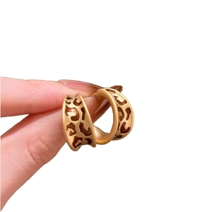 Boucles d'oreilles créoles dorées en C avec motif léopard ajouré tenues par les doigts