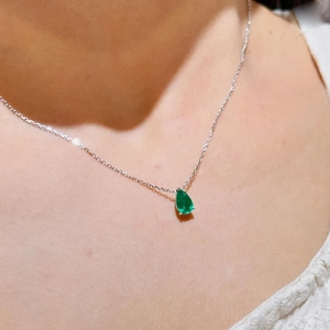 Detailed view of pear-shaped green emerald pendant on silver chain worn by a model
