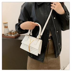 Detail of white leather handbag featuring gold V-shaped buckle and chain tassel on model