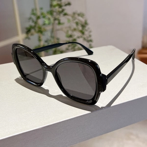 Detail view of stylish black oversized sunglasses on a textured grey display stand