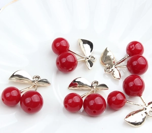 Detailed view of red resin cherry pendants with gold leaves on a white ceramic plate