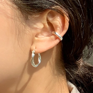 Macro view of woven sterling silver hoop earrings and polished ear cuff worn on the ear