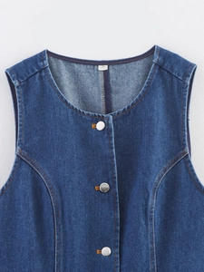 Détail du gilet en jean bleu montrant des boutons métalliques et des surpiqûres orange