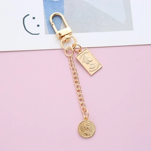 Macro detail of golden keychain with Queen Elizabeth II coin charms on pink background