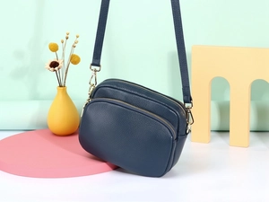 Detailopname van donkerblauwe crossbodytas van generfd leer met gouden metalen details