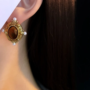 Gros plan d'une boucle d'oreille ovale dorée vintage avec pierre brune et perles