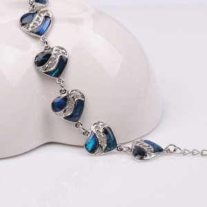 Macro shot of silver heart link bracelet with blue shell inlay on white ceramic plate