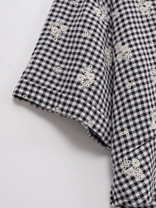 Détail de broderie florale blanche sur la manchette d'une chemise à carreaux