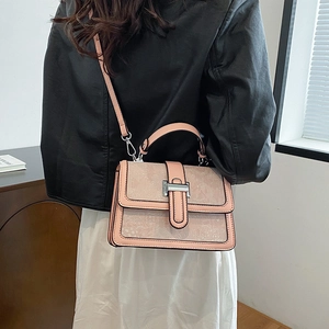 Detailed side view of peach textured crossbody bag with silver H-buckle on model