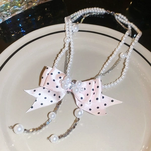 Detail of pink polka dot bow and multilayer pearl necklace on a white ceramic tray