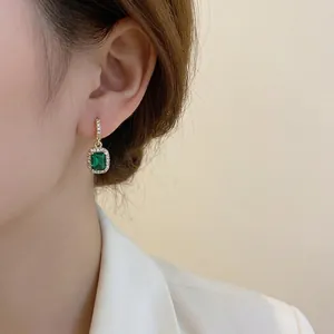 Elegant emerald green square drop earrings with diamond halo worn by model