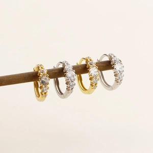 Detail of silver and gold hoop earrings set with zircon on a neutral wooden display