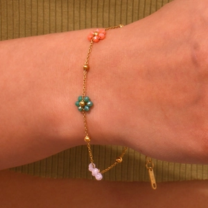 Detail of beaded floral bracelet in pink, green and purple on a golden chain