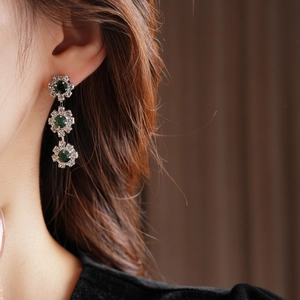 Close-up of silver sunflower earrings featuring green center stones and crystal petals