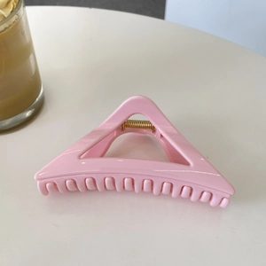 Close-up of pink 12cm triangular hair claw clip with golden metal spring on white desk