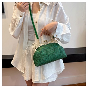 Detail view of a vintage dark green shell bag with embossed floral texture and gold handle