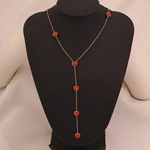 Detail of a gold Y-shape necklace with red glass heart pendants on a black mannequin