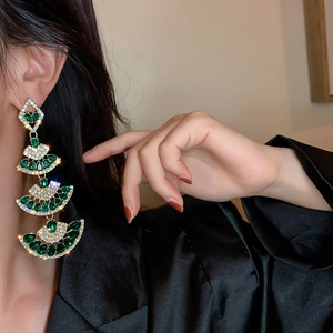 Detail view of long fan-shaped tassel earrings with emerald stones on model