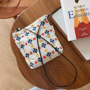 Détail de broderies florales sur un sac bandoulière en lin beige avec sangle noire