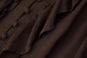 Détail du tissu crêpe marron foncé avec volants superposés et boutons assortis