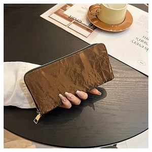 Brown pleated metallic wallet with gold zipper detail held in a lifestyle setting