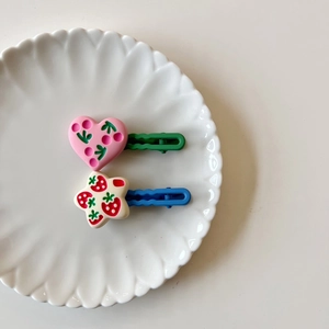 Set of two colorful geometric kids hair clips with heart and star patterns in a white dish