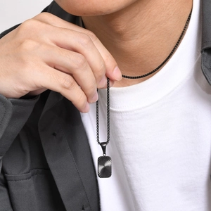 Close-up of men's matte black rectangular pendant with textured sunburst pattern