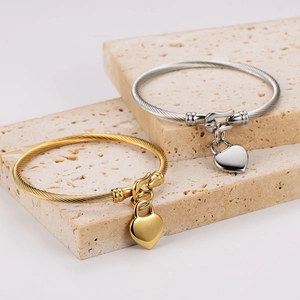 Polished heart pendant cable bangles in gold and silver finish on travertine pedestals