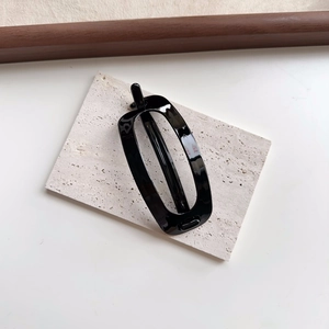 Close-up of a glossy black oval hair clip on a textured white travertine stone surface